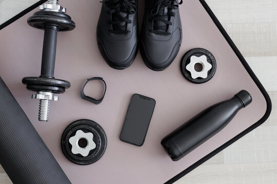 Top view of dumbbells, shoes, water bottle, watch and phone on sport mat