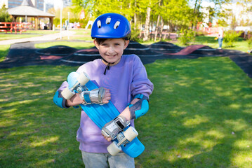 portrait of a smiling schoolboy in a safety helmet with a bright blue skateboard, an urban cruiser...