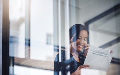 All looks positive from my side. a young businesswoman talking on a cellphone while going through paperwork in an office.