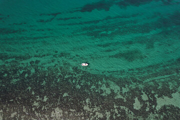 Fototapeta premium One small white boat cruising along the reef in Exmouth, Western Australia. Beautiful turquoise water and corals view from the sky. 