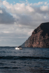 A boat sailing on the sea at sunset with cliffs in the background.