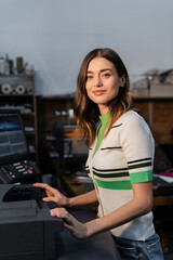 pretty woman looking at camera while standing near professional equipment in print center.