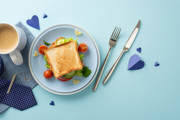 Spoil Dad with a special Father's Day breakfast. Top view of a homemade sandwich with veggies, knife, fork, coffee mug, napkin, necktie clip, men's accessories, on pastel blue background
