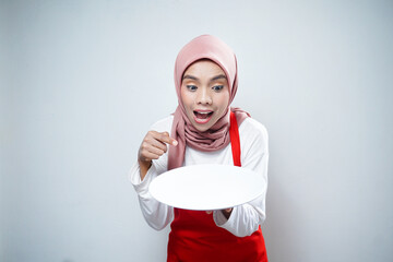 Young Asian muslim woman in apron standing and holding empty white plate isolated on white background