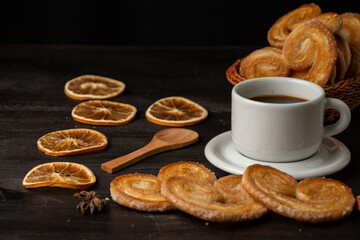 View of puff pastry with dried oranges and cup of coffee on dark wooden table, horizontal with copy space