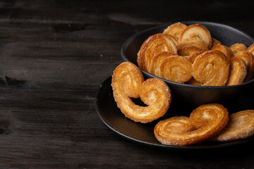 Top view of puff pastries in black bowl on dark table, selective focus, horizontal, with copy space