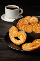 Top view of puff pastry in black bowl on dark table with cup of coffee, selective focus, vertical, with copy space