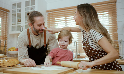 Father and mother teaching baby son kneading dough on kitchen counter at home. Parents and boy kid enjoy and fun indoors activity cooking together.