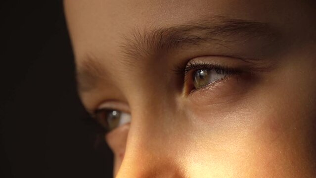 Close-up of the kid eyes. A dreaming boy looks in the dark, a ray of light falls on his eyes. happy childhood, dreams. Side view
