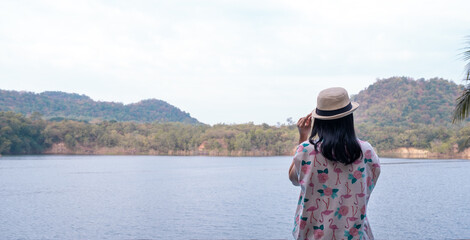 Obraz premium Asian woman with hat standing and enjoying the morning scenery by the lake with mountains