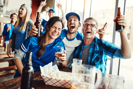 The bar is where its all going down. a group of friends cheering while watching a sports game at a bar.