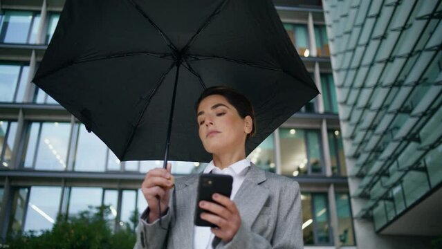 Elegant worker texting phone under umbrella. Downtown employee make online order