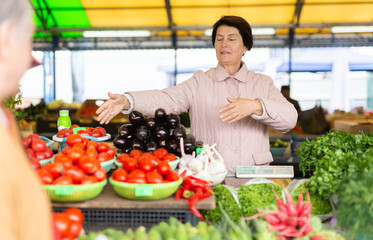 Aged woman customer buying vegetables in open-air market