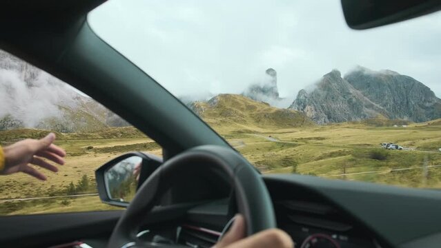 Traveler is driving a car through a mountain pass in the Alps while using a digital map for navigation. They are enjoying the drive and sticking their arm out the window, creating waves with their