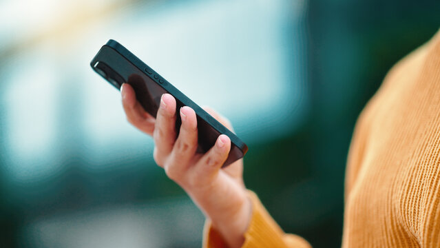 Closeup female entrepreneurs hands texting on a phone outside standing in a park with bokeh lights. Businesswoman browsing online and typing emails on mobile technology while using an app outside - Powered by Adobe