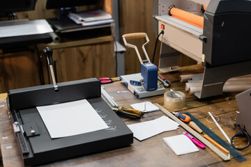 blank paper on top of paper trimmer machine next to different tools in modern print center.