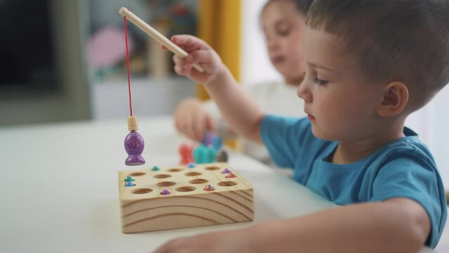 children at the table in kindergarten play an educational game fishing. development of fine dream motor skills in children. children play educational game catch fish in kindergarten. game kid concept