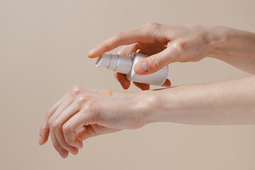 Female hands applying texture of serum or lotion on skin on beige isolated background close-up. The...