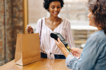 Female ceramic store owner swiping a credit card while serving a customer