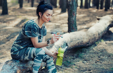 Fit woman drinks amino acids and has a protein bar in the forest