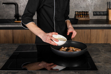 A Cook in a black uniform in the kitchen with ingredients prepared for cooking. Chef making an omelet with bacon for breakfast.