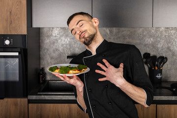 A satisfied and pleased Cook in a black uniform in the kitchen with his dish. Chef with a healthy breakfast.
