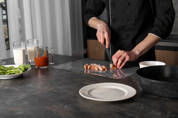 A Cook in a black uniform in the kitchen with ingredients prepared for cooking. Chef making an omelet with bacon for breakfast, slicing meat on a cutting board.