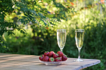 Glasses of champagne and strawberries on a table in a summer garden against the backdrop of evening...