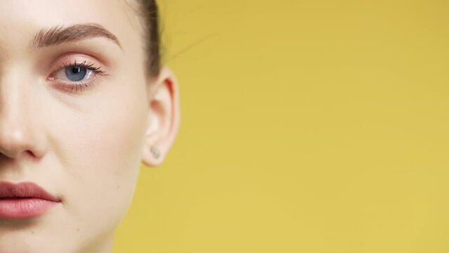 Half face of young pretty woman with european appearance on yellow, copy space