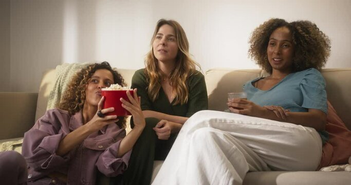 Portrait of Happy Group of Female Friends Watching a Funny Show and Laughing in Cozy Living Room. Flatmates Having a Movie Night at Home, Eating Popcorn and Enjoying Their Evening Together