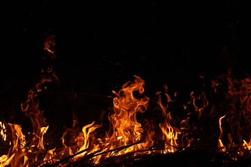Burning red hot sparks fly from large fire in the night sky. Fire flames with sparks on the night...