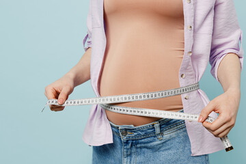 Cropped young pregnant future mom woman with belly tummy with baby wearing casual clothes hold measure tape on belly check growth isolated on plain pastel blue background. Maternity pregnancy concept.