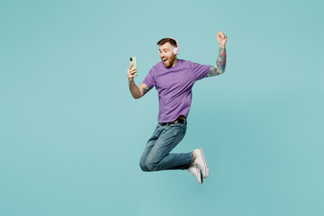 Full body side view young man he wears purple t-shirt headphones listen music jump high hold in...
