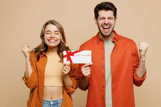 Young couple two friends family man woman wear casual clothes looking camera together hold gift certificate coupon voucher card for store do winner gesture isolated on pastel plain beige background.