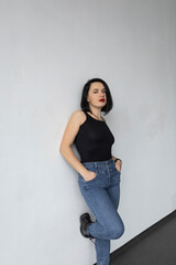 Woman with black hair, maida and jeans standing near the white wall