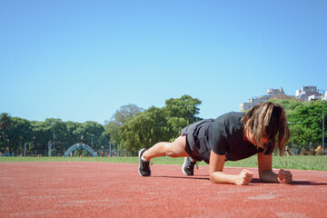 young latin woman training doing plank muscle crunch on the running track.