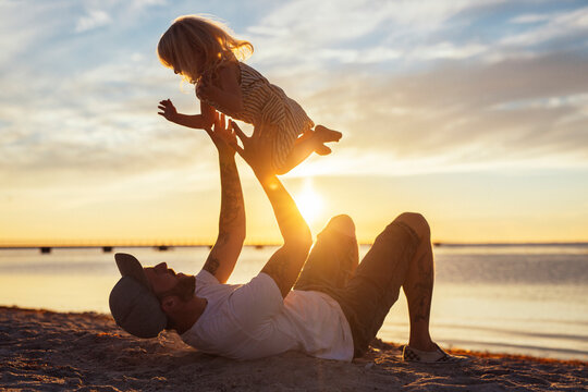 Father tossing daughter (2-3) on beach