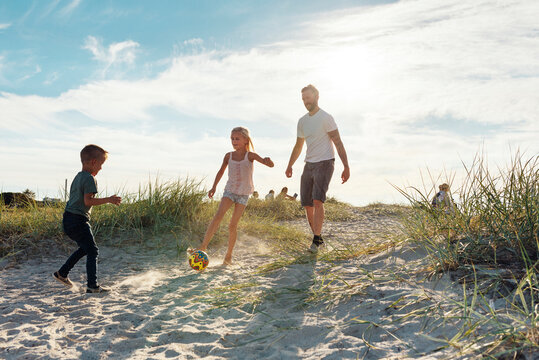 Father kicking ball with children (4-5, 8-9) on beach