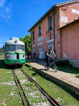 Un ragazzo in bicicletta pedala in una stazione , sullo sfondo un trenino vintage