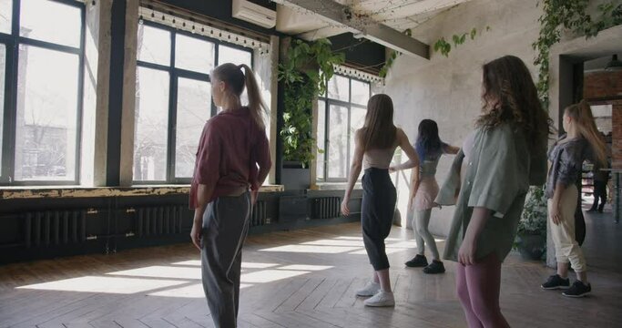Female dancers moving to music learning new hip hop dance in modern sunlit studio. Stylish young people and contemporary culture concept.