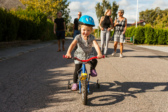 Girl (2-3) riding bicycle, family in background