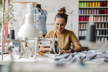 Fashion designer using a sewing machine at her workplace
 - obrazy, fototapety, plakaty