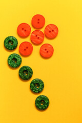 Daisy flower made from orange and green plastic buttons on a yellow background. Top view. Copy space.