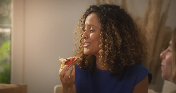 Portrait of Young Multiethnic Brazilian Woman Eating Pizza and Chatting with Friends at Home in Cozy Sunny Living Room. Beautiful Girl with Curly Hair Enjoying Food From Local Business Restaurant