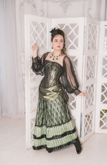 Beautiful young smiling woman wearing green medieval vintage Victorian Style dress stand near screen