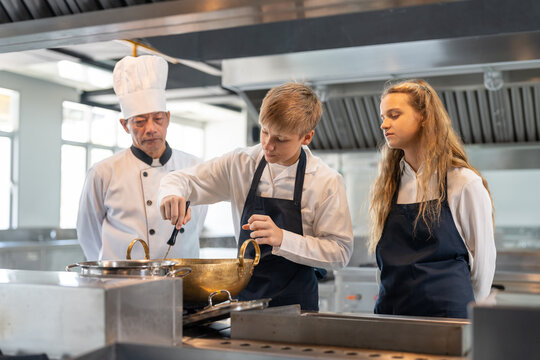 Group of student boy and girl studying cooking in class at school kitchen. Senior Asian teacher chef teaching cooking to children. Education Concept