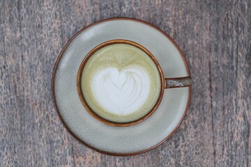 Flat lay or top view shot of a cup of Matcha Latte with beautiful Latte Art on a wooden table