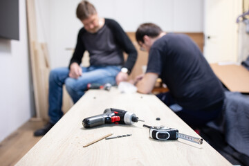 Low viewing angle elderly father and son assemble furniture at home on their own. in blurred focus, selective focus. Tools for assembling a shelf, a drill, an electric screwdriver, a measuring tape 
