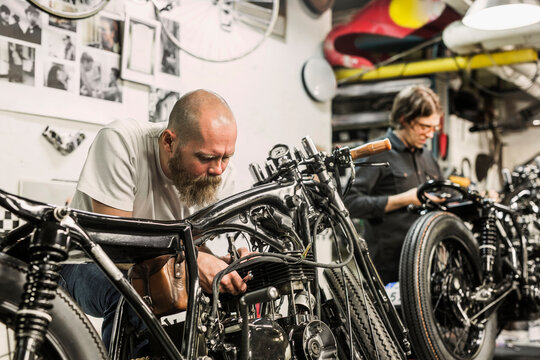 Two men repairing retro motorcycles in workshop