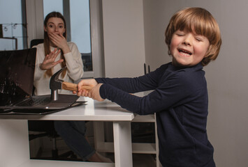 Happy child smashes mom's work laptop to spend more time together. The toddler laughs because he...